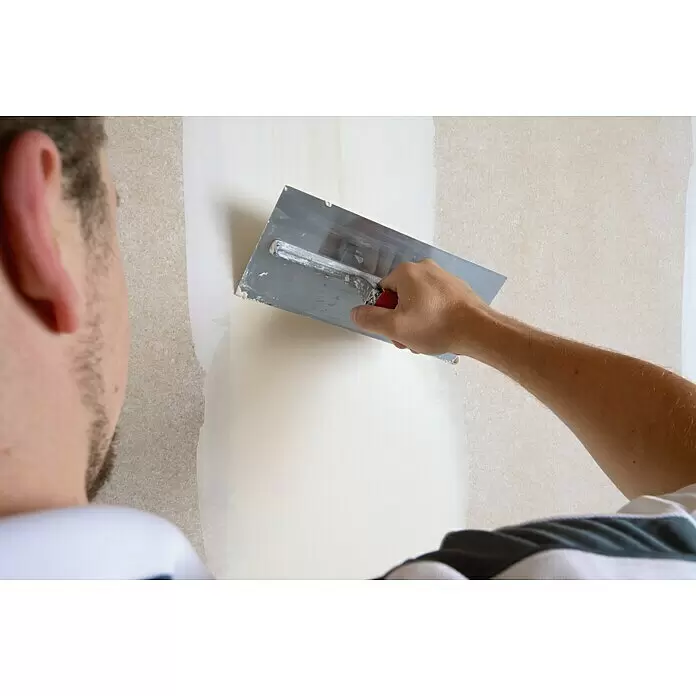 Rigips Rigidur Glasgewebeband - 50 m x 70 mm - Hand trägt weißen Putz mit einer Glättkelle auf eine Wand auf.