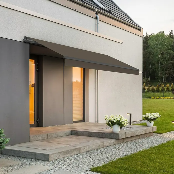 SmartSun Gelenkarmmarkise ClassicTaupe, Breite: 3,95 m, Ausfall: 2,5 m - Moderne Hausfassade mit grauer Markise über dem Eingangsbereich und stilvoller Beleuchtung für ein einladendes Ambiente.