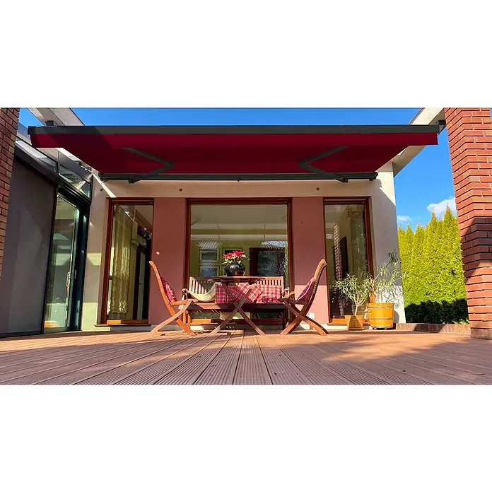 SM Hülsenmarkise T-407/11 - Rot, Farbe Gestell: Anthrazitgrau, Breite: 2,5 m, Ausfall: 2 m - Eine rote Markise spendet Schatten über einer Terrasse mit Holzboden, Sitzgruppe und Pflanzen, ideal für entspannte Stunden im Freien.