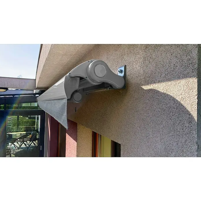 SM Hülsenmarkise T-5406/107 - Grau, Farbe Gestell: Weißaluminium, Breite: 3,6 m, Ausfall: 2,5 m - Detailansicht einer eleganten, ausfahrbaren Markise, die an einer Wand montiert ist und Schatten spendet.