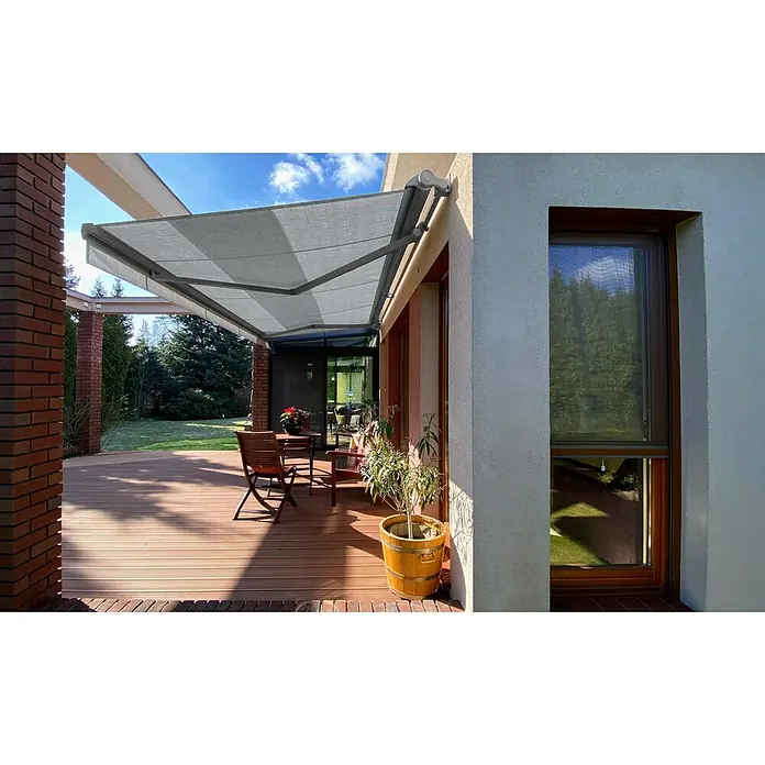 SM Hülsenmarkise REC-196 - Hellgrau, Farbe Gestell: Weißaluminium, Breite: 5 m, Ausfall: 3 m - Eine ausfahrbare Markise spendet Schatten auf einer Terrasse mit Holzdeck und Sitzgelegenheiten, ideal für entspannte Stunden im Freien.