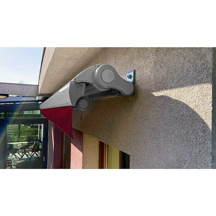 SM Hülsenmarkise T-407/11 - Rot, Farbe Gestell: Weißaluminium, Breite: 3,6 m, Ausfall: 2,5 m - Nahaufnahme einer grauen Markise mit rotem Volant, befestigt an einer getexturieren Wand, die Schatten wirft, für Sonnenschutz.