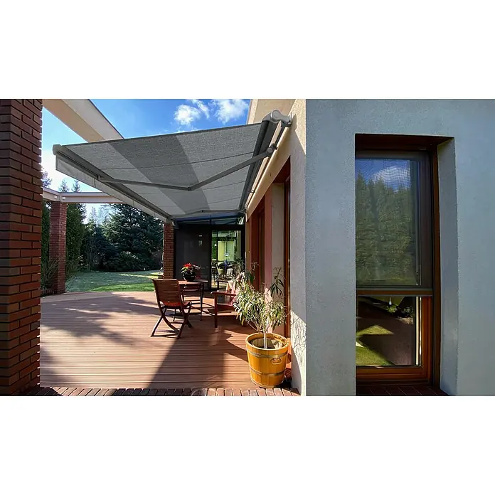 SM Hülsenmarkise T-5406/107Grau, Farbe Gestell: Weißaluminium, Breite: 5 m, Ausfall: 3 m - Eine graue Gelenkarmmarkise spendet Schatten über einer Terrasse mit Holzboden, die mit einem Tisch und Stühlen möbliert ist.