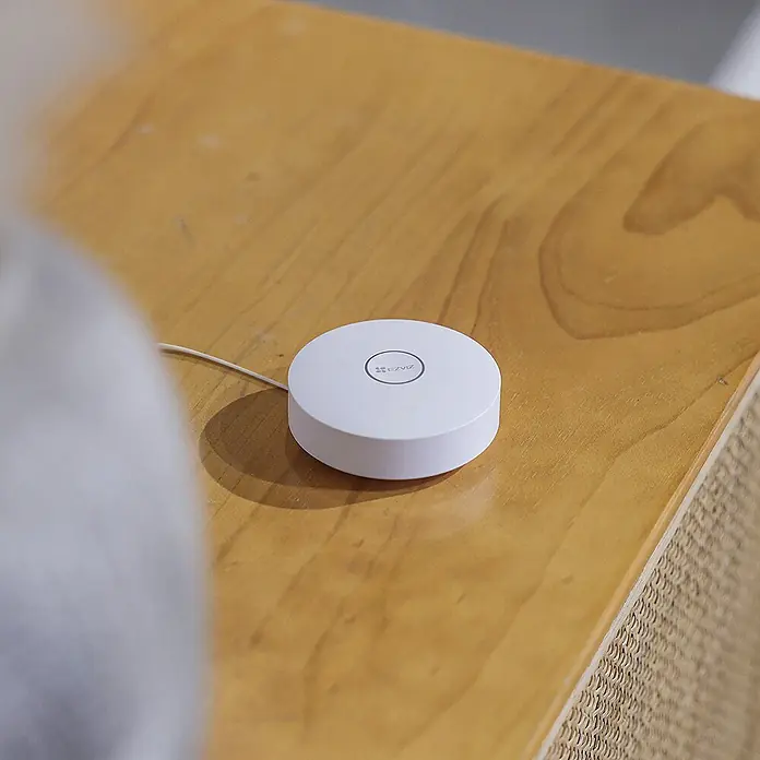 EZVIZ Set de cerradura electrónica con teclado y puerta de enlace A3 - 3 pzs. - Primer plano de un hub inteligente EZVIZ blanco sobre una mesa de madera, que ofrece tecnología moderna y comodidad para el hogar.