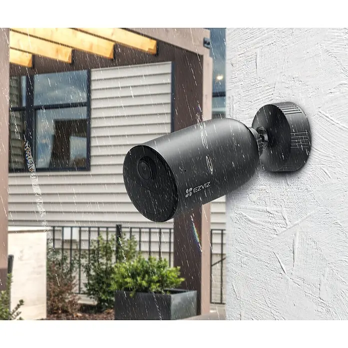EZVIZ Cámara de vigilancia EB3 - Negro - Una cámara de seguridad EZVIZ resistente a la intemperie en negro está montada en una pared blanca, grabando bajo la lluvia.