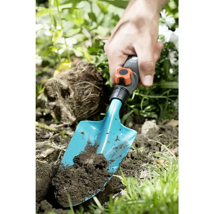 Gardena Combisystem Blumenkelle - Arbeitsbreite: 8,5 cm, Stahl - Nahaufnahme eines Gärtners, der mit einer hellblauen Gartenschaufel Erde aushebt, um eine Pflanze einzusetzen.