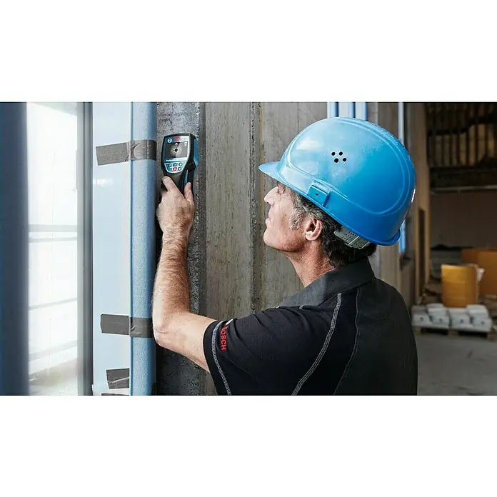 Bosch Professional Ortungsgerät D-Tect 120 - Ohne Akku, Erfassungstiefe: Max. 38 mm Holzunterkonstruktionen - Ein Bauarbeiter mit Schutzhelm benutzt ein Bosch-Ortungsgerät, um versteckte Objekte in einer Wand zu finden. Das Gerät ist gut sichtbar.