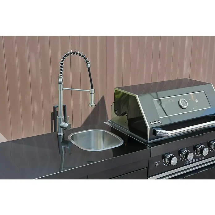 Buschbeck Outdoorküche Cambridge - Schwarz, Material Grillfläche: Edelstahl, Anzahl Brenner: 4 - Detaillierte Ansicht eines Buschbeck Outdoor-Küchenmoduls mit Spüle und modernem Wasserhahn neben einem Grill.