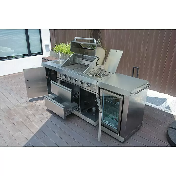 Buschbeck Outdoorküche Oxford - Edelstahl, Anzahl Brenner: 4 - Outdoor-Küche aus Edelstahl mit Gasgrill, Spüle, Schubladen und Getränkekühlschrank auf einer Holzterrasse.
