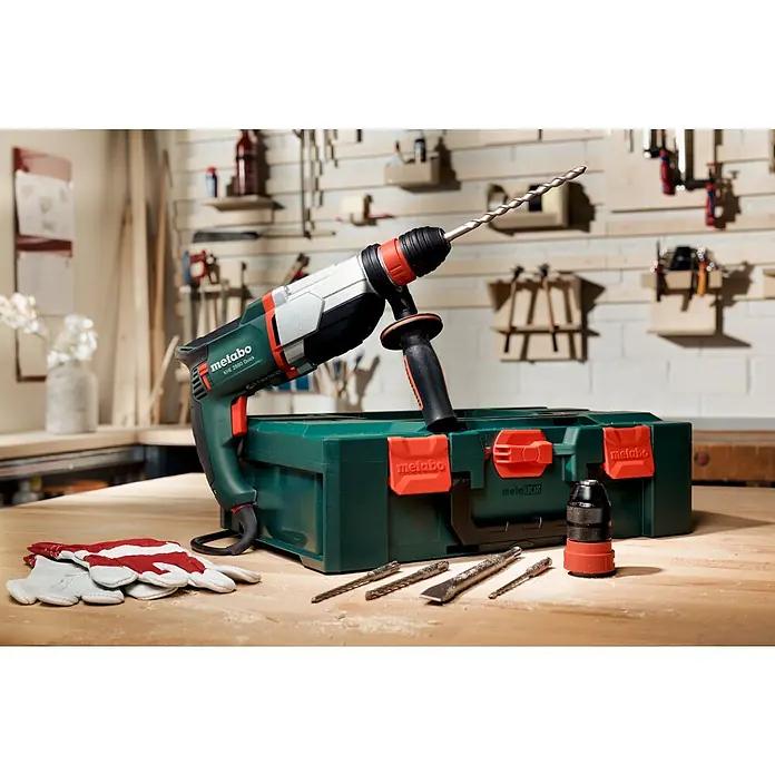 Metabo Kombihammer KHE 2860 Quick Set - 880 W, 3,2 J, SDS-Plus-Aufnahme - Nahaufnahme einer Metabo KHE 2680 Quick Bohrmaschine mit Zubehör, die auf einem Holztisch mit Werkzeugen und Handschuhen platziert ist.