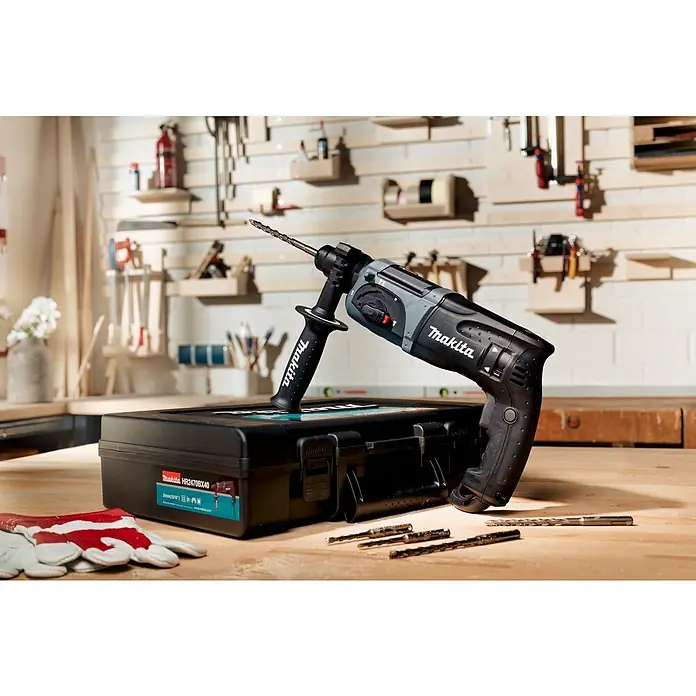 Makita LXT 18V Taladro atornillador de batería DDF482RFJ - 18 V, Sin batería - Primer plano de un martillo perforador Makita HR2470BX40 con accesorios y caja de herramientas sobre una mesa de madera contra una pared de herramientas.