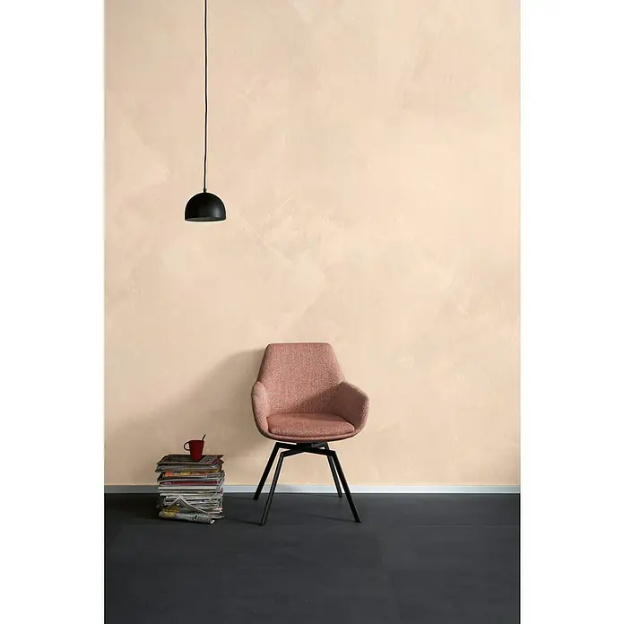 SCHÖNER WOHNEN-Farbe Trendstruktur Farbeffektputz Stone-Optik Effektlasur - Sandstein, Matt, 1 l - Einrichtungsszene mit rosafarbenem Drehstuhl, Bücherstapel und Hängelampe vor beiger Wand. Der Stuhl ist der Mittelpunkt des minimalistischen Designs.