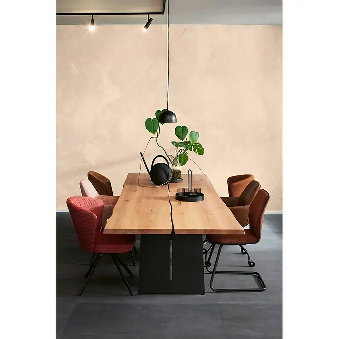 SCHÖNER WOHNEN-Farbe Trendstruktur Dekoputz-Basis Stone-Optik Grundfarbe - Sandstein, 2,5 l - Esszimmertisch aus Holz mit schwarzen Beinen, umgeben von farbigen Stühlen, mit Dekorationen wie einer Gießkanne und einer Hängelampe.