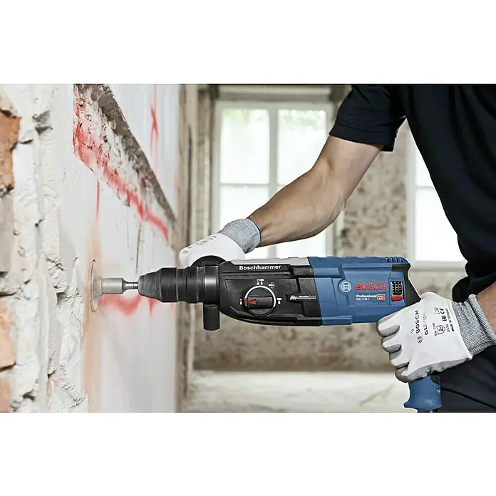 Bosch Professional Kombihammer GBH 2-28 F - 880 W, 3,2 J, SDS-Plus-Aufnahme, Inkl. 3 x Bohrer & Meißel - Ein Arbeiter benutzt einen Boschhammer, um ein Loch in eine Wand zu bohren. Der Boschhammer ist blau und schwarz.