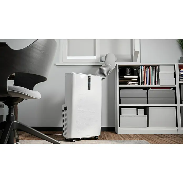 Voltomat Mobiles Klimagerät WiFi 12.000 BTU - 3.500 W, Raumgröße: 35 m², Weiß - Tragbare Klimaanlage mit Abluftschlauch am Fenster, steht neben einem Regal und einem Schreibtischstuhl.