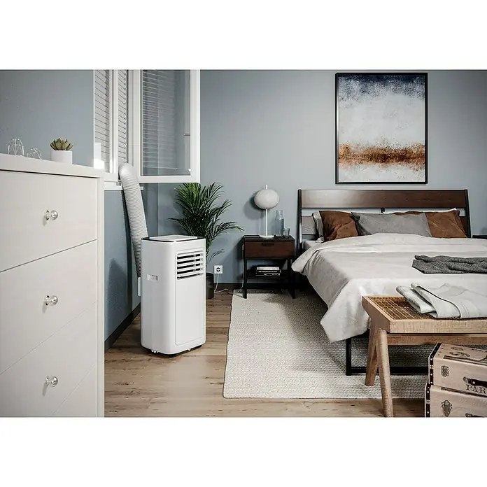 Voltomat Aire acondicionado portátil Boreas - 2.000 W, Tamaño de la estancia: 20 m², Blanco/Negro - Un dormitorio moderno con un aire acondicionado portátil blanco conectado a una ventana, diseñado para crear un ambiente confortable.