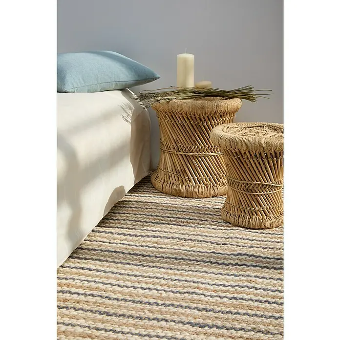 Alfombra de yute Rayas - Natural/crudo, 150 x 80 cm - Primer plano de dos taburetes decorativos de mimbre sobre una alfombra de rayas, junto a una cama con almohada azul.