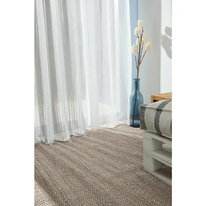 Alfombra de yute Córdoba - Gris, 230 x 160 cm, 100% yute - Primer plano de una alfombra beige texturizada frente a una ventana con cortinas blancas y un jarrón azul decorativo.