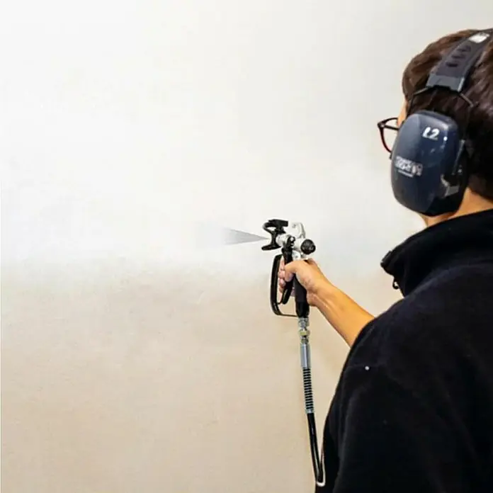 Scheppach Farbsprühsystem PTSA350 - 750 W, Förderleistung: 1,1 l/min - Ein Mann sprüht Farbe mit einer Farbspritzpistole auf eine Wand, er trägt Kopfhörer. Die Spritzpistole ist das Hauptaugenmerk.