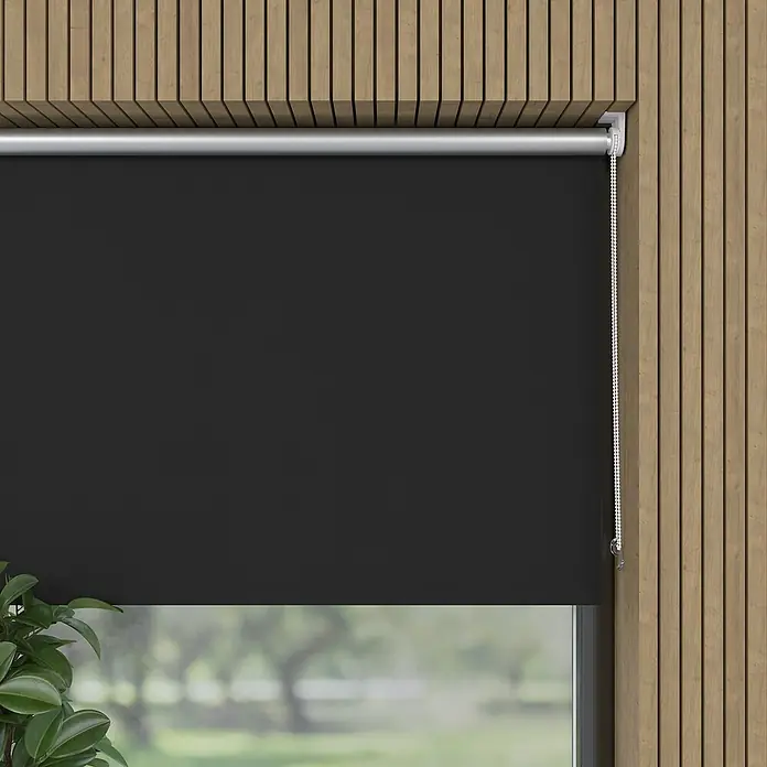 Expo Ambiente Rollo Mini - B x H: 100 x 150 cm, Schwarz, Uni, Verdunkelnd - Das Bild zeigt eine verdunkelnde Rollo mit silberner Kette vor einem Fenster mit Blick ins Grüne. Die Rollo ist vollständig heruntergelassen.