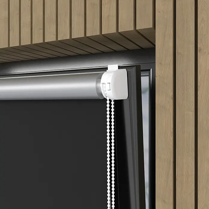 Expo Ambiente Rollo Mini - B x H: 100 x 150 cm, Schwarz, Uni, Verdunkelnd - Nahaufnahme einer schwarzen Verdunkelungsrollo mit weißer Bedieneinheit und Kugelkette vor einer Wand mit Holzpaneelen.