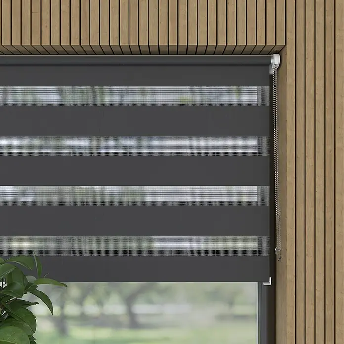 Expo Ambiente Doppelrollo Mini - B x H: 60 x 150 cm, Grau - Eine moderne, graue Doppelrollo, die vor einem Fenster mit Holzrahmen hängt, bietet sowohl Lichtschutz als auch Privatsphäre.