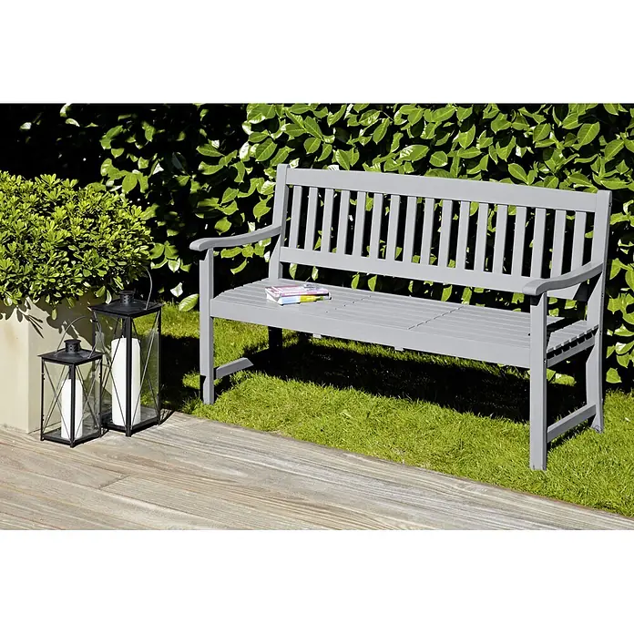 Sunfun Gartenbank Corinna - B x T x H: 150 x 64 x 92,5 cm, Hartholz, Hellgrau - Eine graue Gartenbank aus Holz steht auf einer Terrasse neben einer Hecke und Laternen, ideal zum Entspannen im Freien.