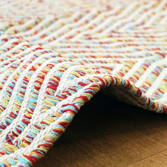 Kayoom Flachgewebeteppich Cocktail 400Bunt, 150 x 80 cm, 100% Baumwolle - Detailaufnahme eines farbenfrohen Teppichs mit geflochtenen Akzenten und einem hellen, einladenden Design.