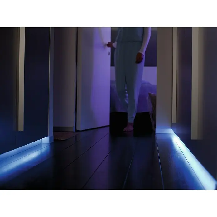 Philips Hue LED-Band Plus Basis - 2 m, RGBW - Das Bild zeigt einen dunklen Flur mit blauer LED-Beleuchtung am Boden, die eine moderne und stimmungsvolle Atmosphäre schafft.