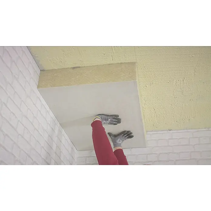 Rockwool Steinwolle Planarock Top 35 KellerdeckendämmungStärke: 120 mm, Wärmeleitfähigkeit: 0,034 W/(mK) - Eine Person befestigt eine graue Akustikplatte an einer Decke, um Schall zu absorbieren und die Raumakustik zu verbessern.