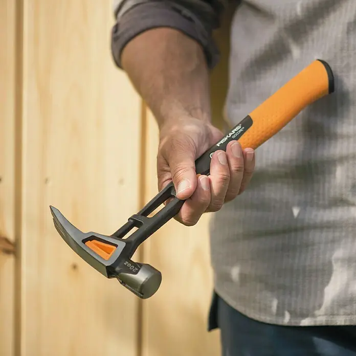 Fiskars Universalhammer M - Gewicht Kopf: 450 g, Länge: 340 mm - Nahaufnahme eines Mannes, der einen orangefarbenen Fiskars-Hammer hält, der sich ideal für Reparaturen, Bauarbeiten und Heimwerkerprojekte eignet.