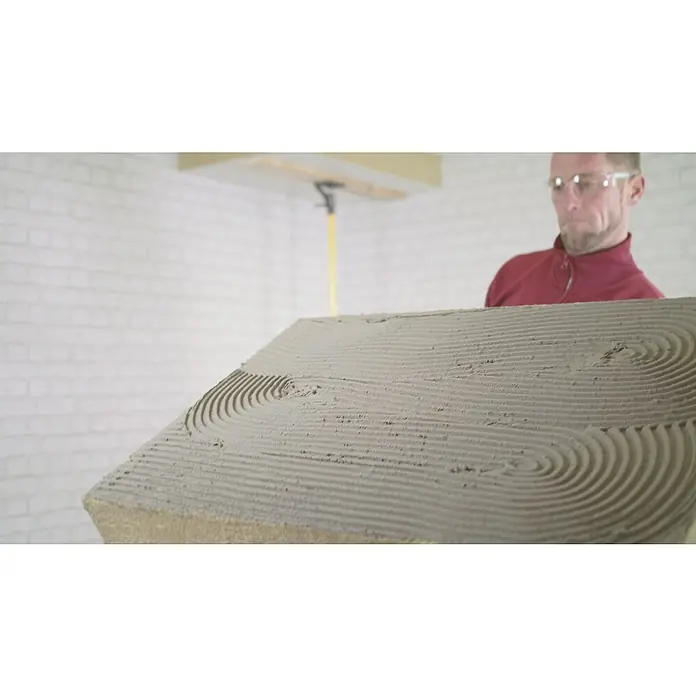 Rockwool Steinwolle Planarock Top 35 KellerdeckendämmungStärke: 120 mm, Wärmeleitfähigkeit: 0,034 W/(mK) - Detailaufnahme einer mit Klebstoff versehenen Dämmplatte, die von einem Handwerker gehalten wird, für die Installation.