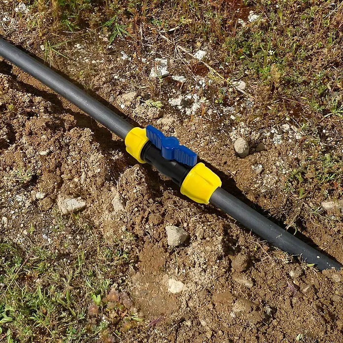 Válvula esférica PE para riego - Diámetro: 25 mm, Polietileno - Primer plano de una manguera de riego negra con accesorios amarillos y una válvula de cierre azul, tendida en el suelo.