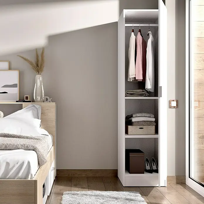 Dekit Armario para ropa Essen - L x An x Al: 52 x 41 x 184 cm, Blanco - Esta imagen muestra un armario blanco y estrecho con una puerta abierta, exhibiendo ropa, mantas y cajas, junto a una cama en un dormitorio.