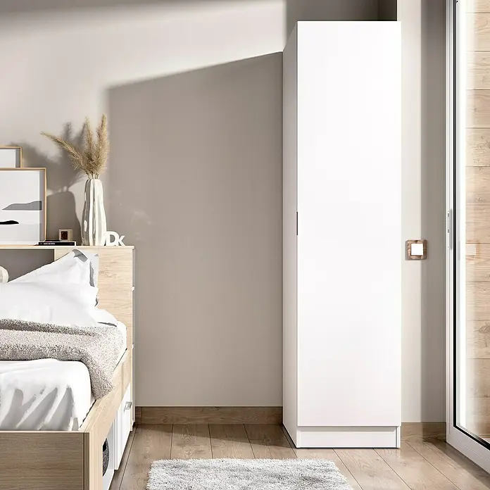 Dekit Armario para ropa Essen - L x An x Al: 52 x 41 x 184 cm, Blanco - Un armario blanco de una puerta se encuentra junto a una cama en un dormitorio. El armario es simple y moderno.