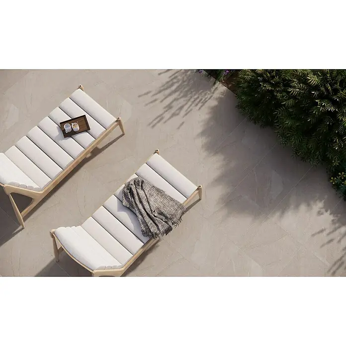 Pavimento cerámico Akane - 45 x 45 cm, Crema, Mate - Dos modernas tumbonas de jardín de madera y tela blanca en un patio con baldosas de piedra, una con manta y la otra con bebidas.