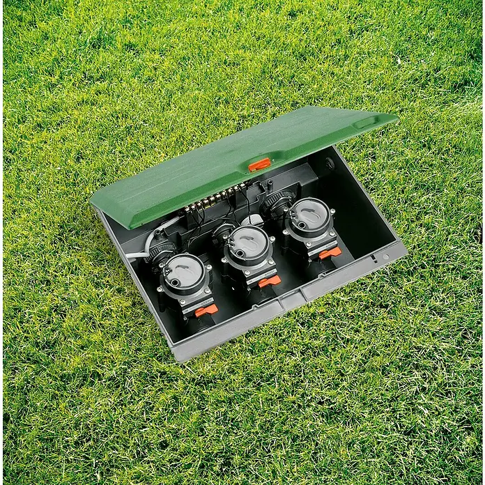 Gardena Sprinklersystem Ventilbox V3 - Passend für: 3 Bewässerungsventile - Bewässerungsanlage mit geöffnetem Deckel auf Rasen. Die Anlage hat drei Regler mit orangen Schaltern zur Bewässerungssteuerung.