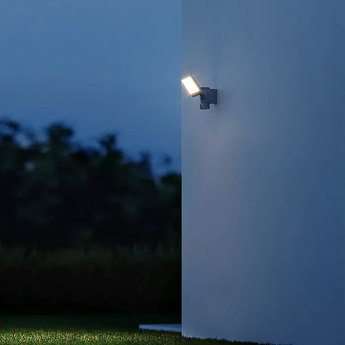 Steinel LED-Strahler CAM 2 SC - 21 W, 2.310 lm, 3.000 K, IP44 - Das Bild zeigt eine moderne, graue Außenwandleuchte, die ein warmes, helles Licht abgibt und eine einladende Atmosphäre schafft.