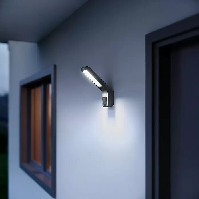 Steinel LED-Sensor-Strahler XLED home Slim S anthrazit - 7,2 W, L x B x H: 201 x 66 x 241 mm, Anthrazit, IP44 - Elegante dunkle LED-Außenwandleuchte mit Bewegungssensor, die eine Hausfassade nachts hell beleuchtet.