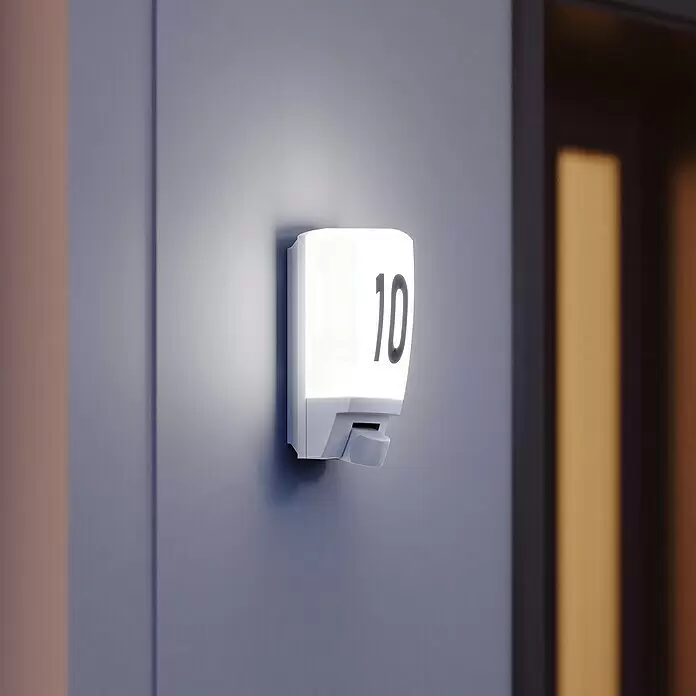 Steinel Sensor-Außenleuchte L 1 S weiß - 60 W, 120 x 110 x 255 mm, Weiß, IP44 - Beleuchtete weiße Hausnummer '10' mit Sensor, an einer Wand neben einer dunklen Tür montiert.