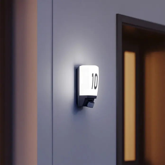 Steinel Sensor-Außenleuchte L 1 S schwarz - 60 W, 120 x 110 x 255 mm, Schwarz, IP44 - Nahaufnahme einer leuchtenden Hausnummer 10 an einer Wand neben einer Tür, die ein modernes und stilvolles Designelement zeigt.