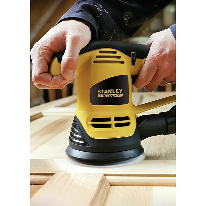 Stanley FatMax Lijadora excéntrica eléctrica FM440K - 480 W - Primer plano de una lijadora orbital amarilla Stanley Fatmax que se utiliza sobre una superficie de madera.