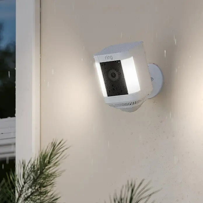 Ring Überwachungskamera Spotlight Cam Plus Battery - Batteriebetrieben, 1.080 Pixel (Full HD), Weiß, B x H: 7,6 x 12,6 cm, Akku - Die Ring Floodlight Cam ist an einer Wand montiert und im Regen zu sehen. Die Sicherheitskamera sorgt für zuverlässige Überwachung.