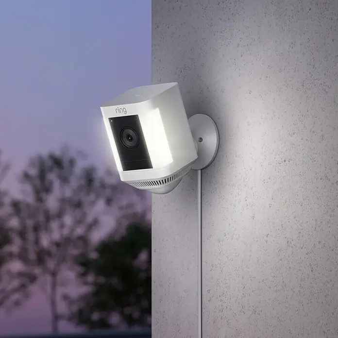 Ring Überwachungskamera Spotlight Cam Plus Plugin - Netzbetrieben, 1.080 Pixel (Full HD), Weiß, B x H: 7,6 x 12,6 cm, Netzanschluss - Eine Ring Sicherheitskamera mit Scheinwerfer an einer Wand befestigt, die für zusätzliche Sicherheit sorgt.