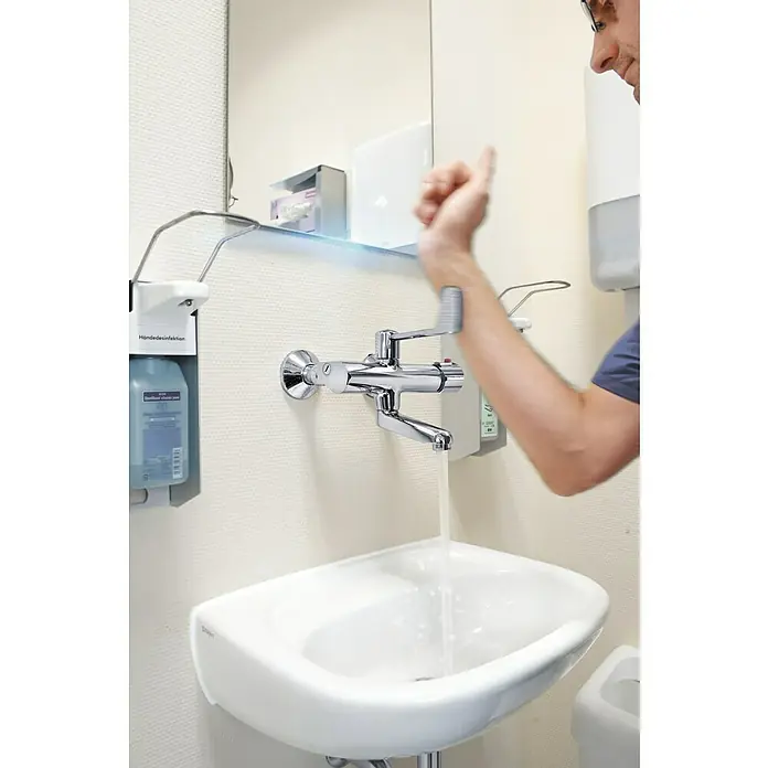 Hansa Tempra Spültischarmatur - Chrom, Glänzend - Ein Waschbecken mit Armatur in einem Badezimmer, an der eine Person mit dem Ellenbogen den Wasserhahn betätigt, um die Hände zu waschen.