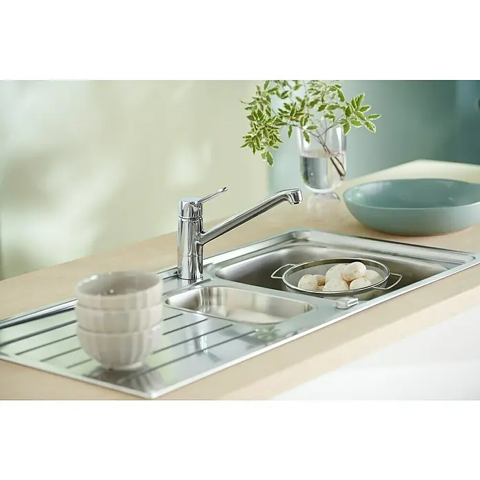 Hansa Primo Spültischarmatur - Niederdruck, Chrom, Glänzend - Nahaufnahme einer Edelstahlspüle mit Wasserhahn, Geschirr und einem Sieb voller Kartoffeln, die eine funktionale und elegante Küchenanordnung zeigt.