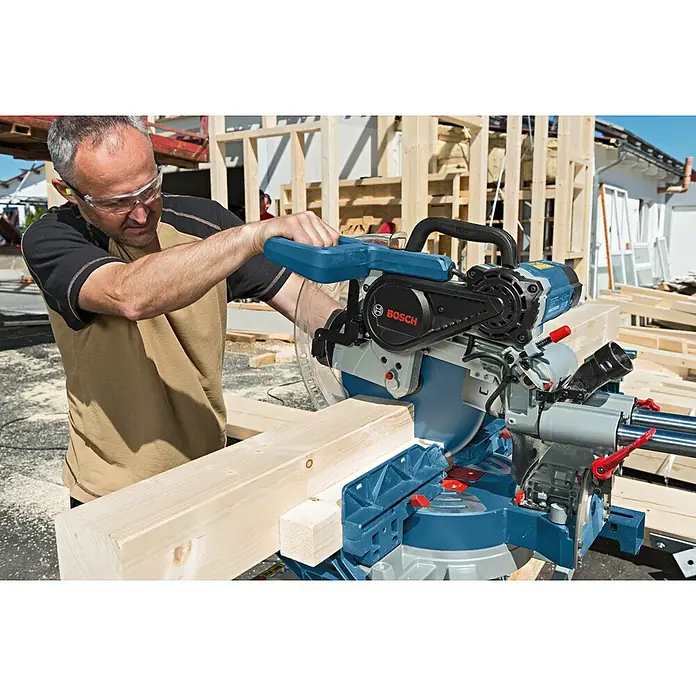 Bosch Professional Sägetisch GTA 2500 W - Belastbarkeit: 180 kg - Ein Mann bedient eine Bosch Kapp- und Gehrungssäge zum Zuschneiden eines Holzstücks vor dem Hintergrund einer Baustelle.