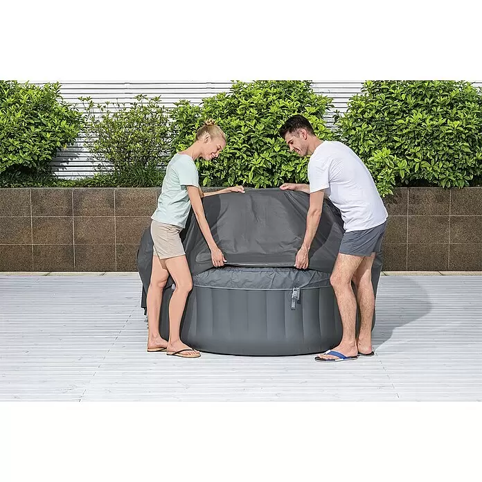 Bestway Lay-Z-Spa Pool-Abdeckplane - Passend für: Runde Whirlpools bis Ø x H: 180 x 66 cm, Ø x H: 180 x 66 cm - Ein Mann und eine Frau nehmen die Schutzabdeckung von einem dunkelgrauen aufblasbaren Whirlpool im Freien.