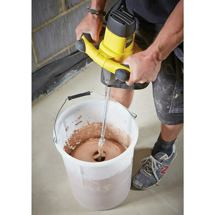Stanley FatMax Mezclador de pintura y mortero FME190 - 1.600 W, Diámetro paleta de mezcla: 150 mm, Volumen de mezcla: 120 l - Un artesano utiliza una mezcladora de mortero Stanley amarilla para remover la mezcla en un cubo.