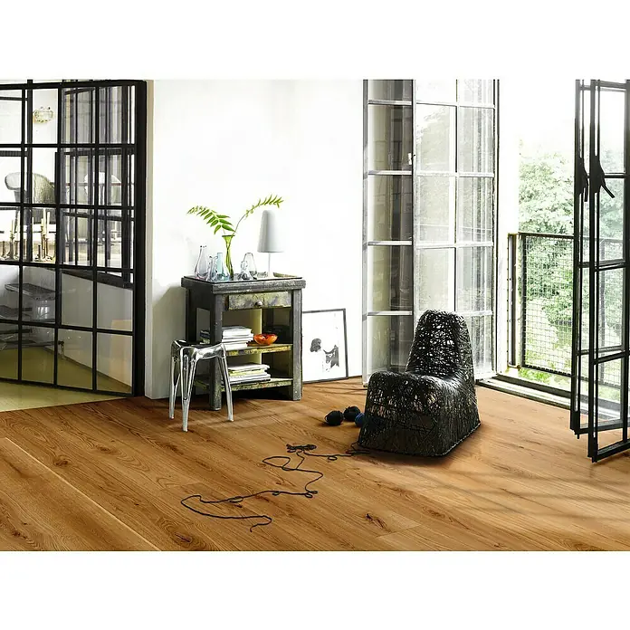 Parador Parkett Basic 11.5 - Eiche gebürstet Naturöl, Landhausdiele, 2.200 x 185 x 11,5 mm - Innenaufnahme eines Zimmers mit Holzboden, einem schwarzen Sessel und einem Beistelltisch, der eine gemütliche und stilvolle Atmosphäre schafft.